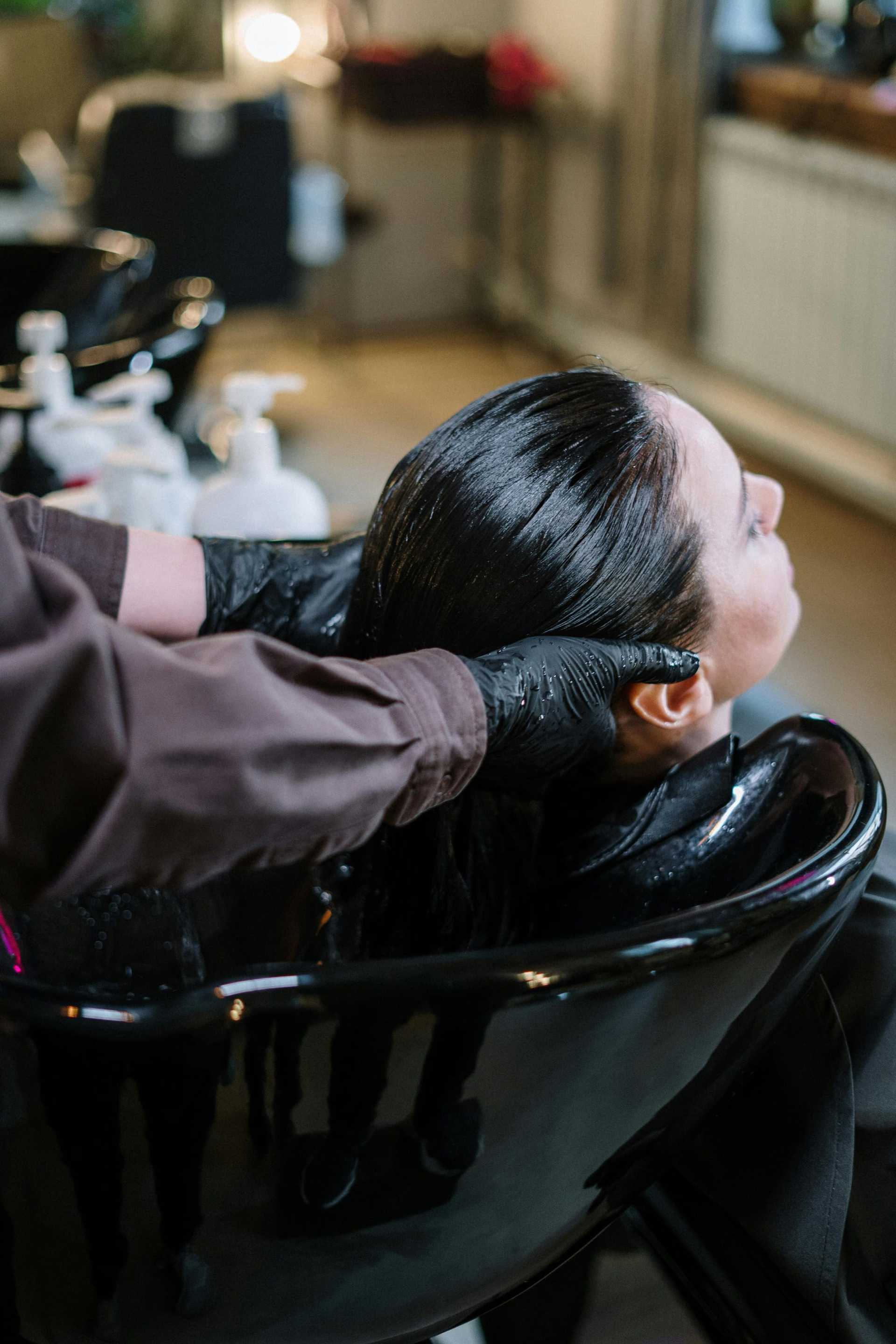 Hairdresser washing client's hair in salon sink.